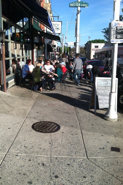 Pedestrians squeeze in between two rows of sidewalks seating.